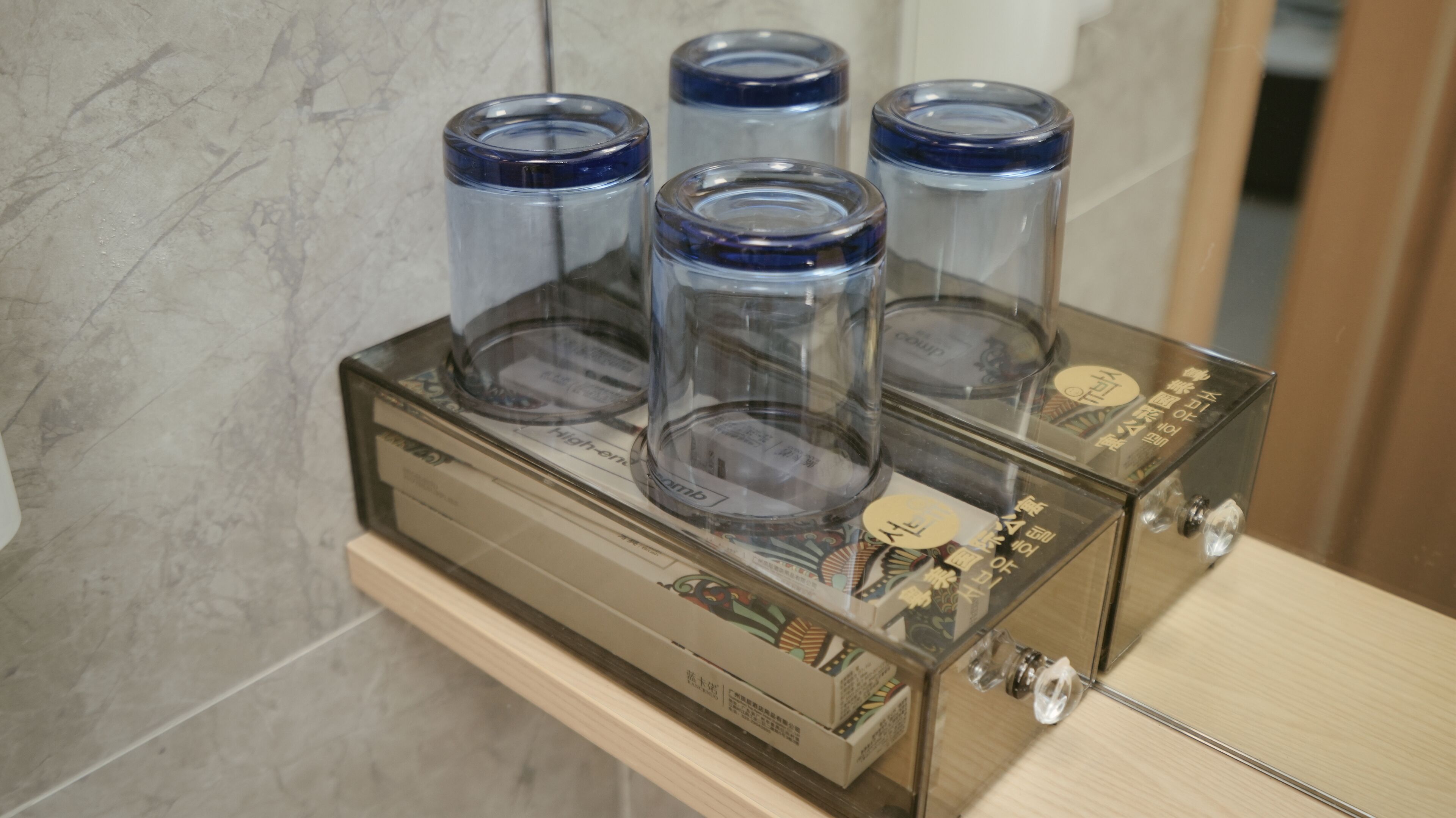 En vattenautomat i glas med fyra behållare som har blå lock och som står på en hylla av trä.