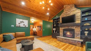 A cozy living room with a stone fireplace, leather sofa, and a flat-screen TV mounted above it.