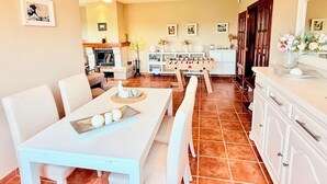 Un coin repas avec une table et des chaises blanches, une cheminée et une table de baby-foot.