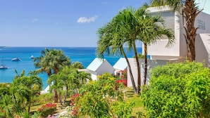 Un hotel costero con edificios blancos, palmeras y barcos al fondo.