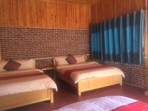A room with two wooden beds, a brick wall, and a window with blue curtains.