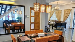 Una moderna zona pranzo con un tavolo rettangolare, sedie rivestite in arancione e illuminazione a sospensione.