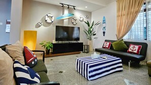 Un soggiorno moderno con una televisione a schermo piatto, un divano, un pouf a righe e un lampadario.