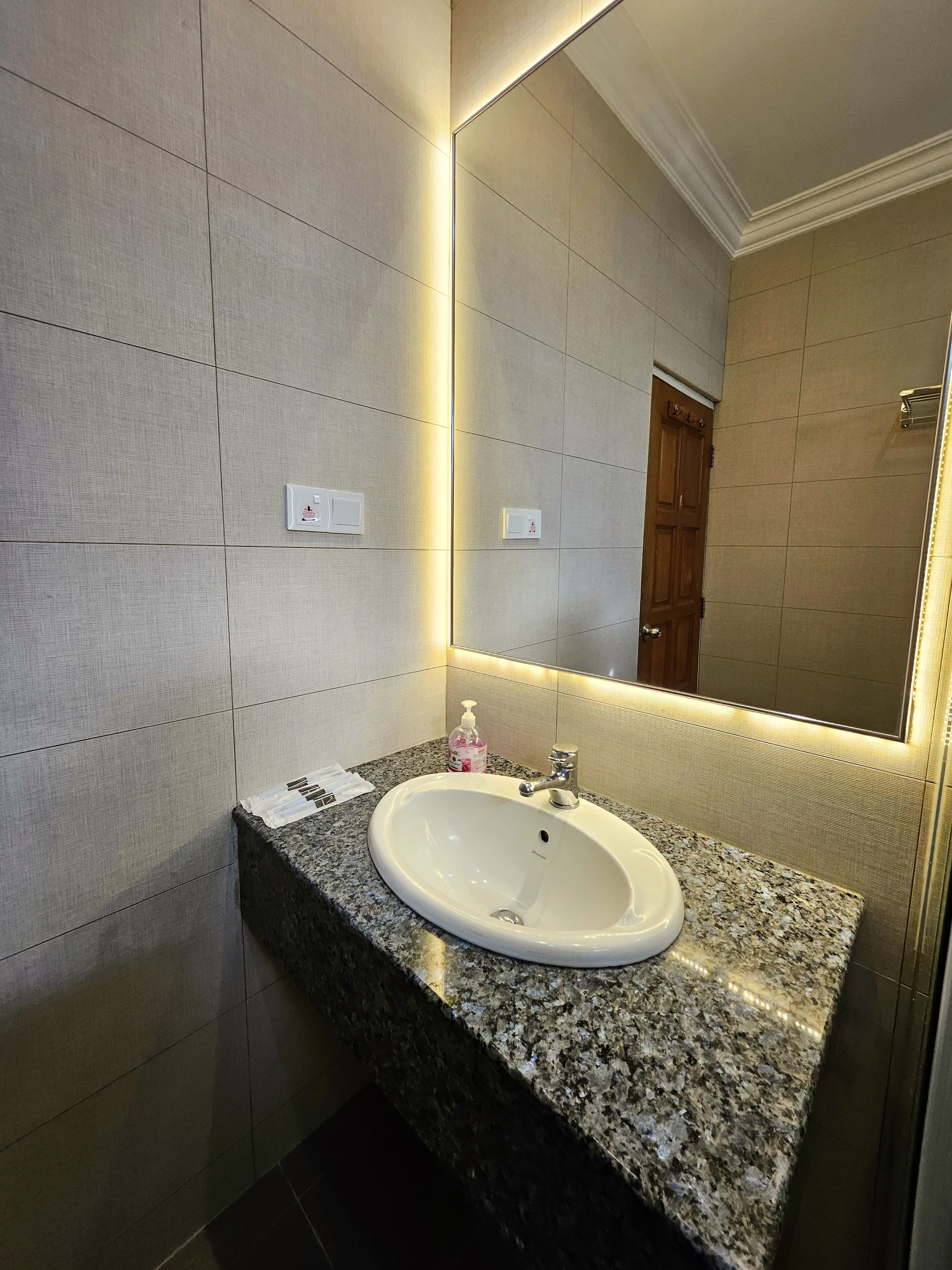 Un baño moderno con encimera de granito, un lavabo blanco y un espejo grande.