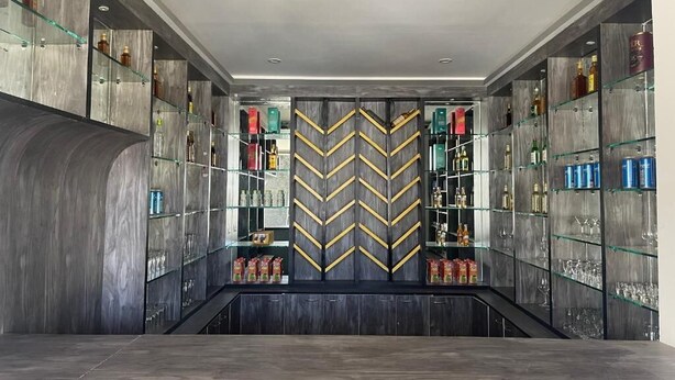 A modern bar area with a central chevron-patterned partition, shelves with bottles, glasses, and snacks. - Yang Bhutan Hotel (Paro)