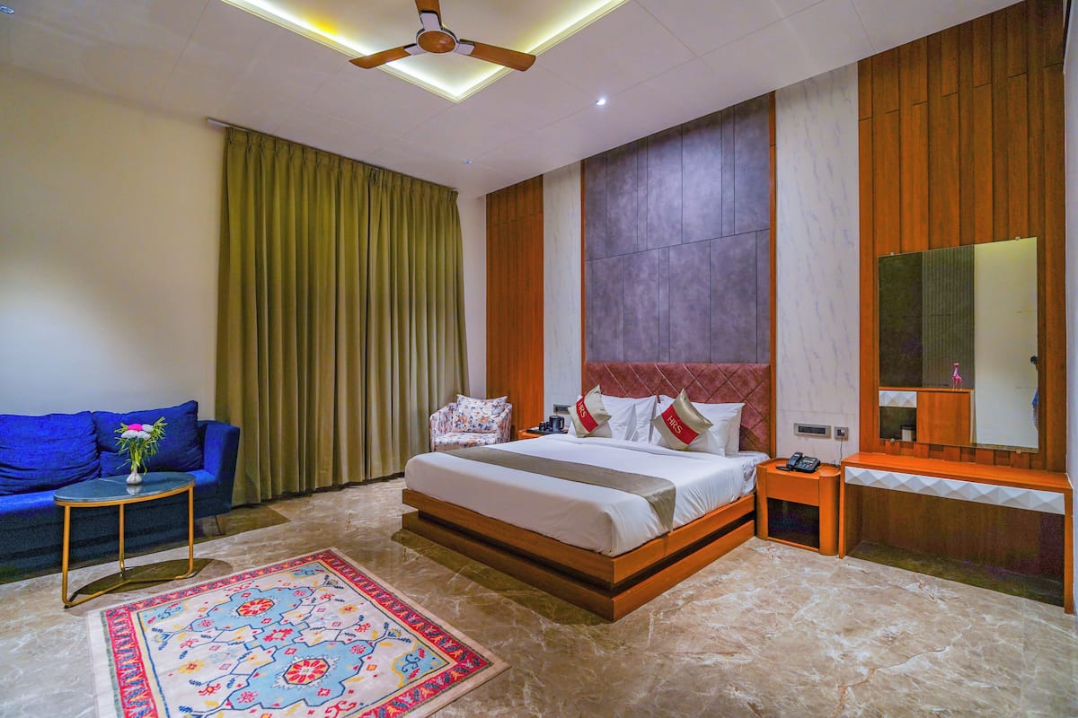 Une chambre d’hôtel avec un grand lit, une table de chevet, un bureau en bois, un canapé bleu et un tapis à motifs.
