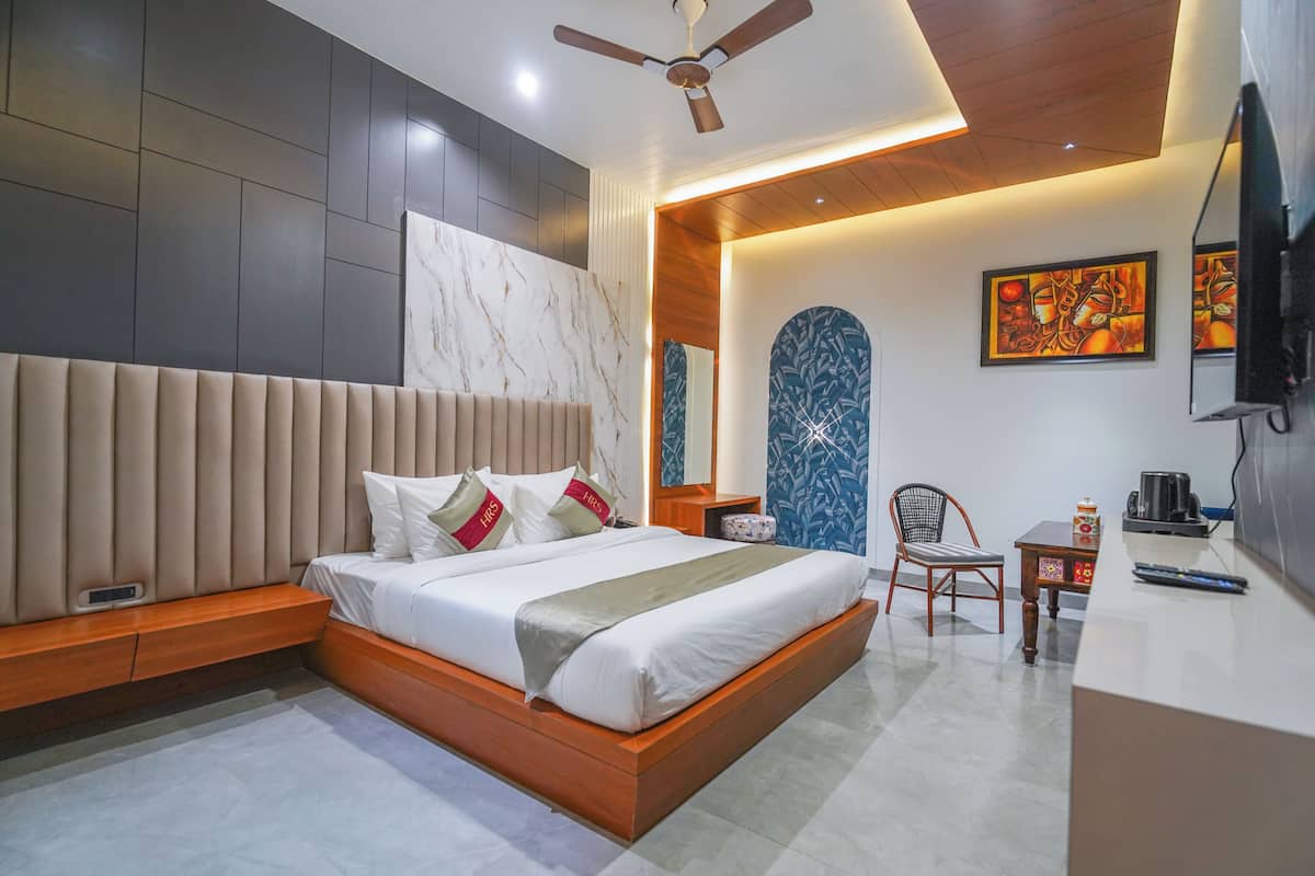 Une chambre moderne avec un grand lit, un ventilateur de plafond, une petite table avec une bouilloire et une chaise.