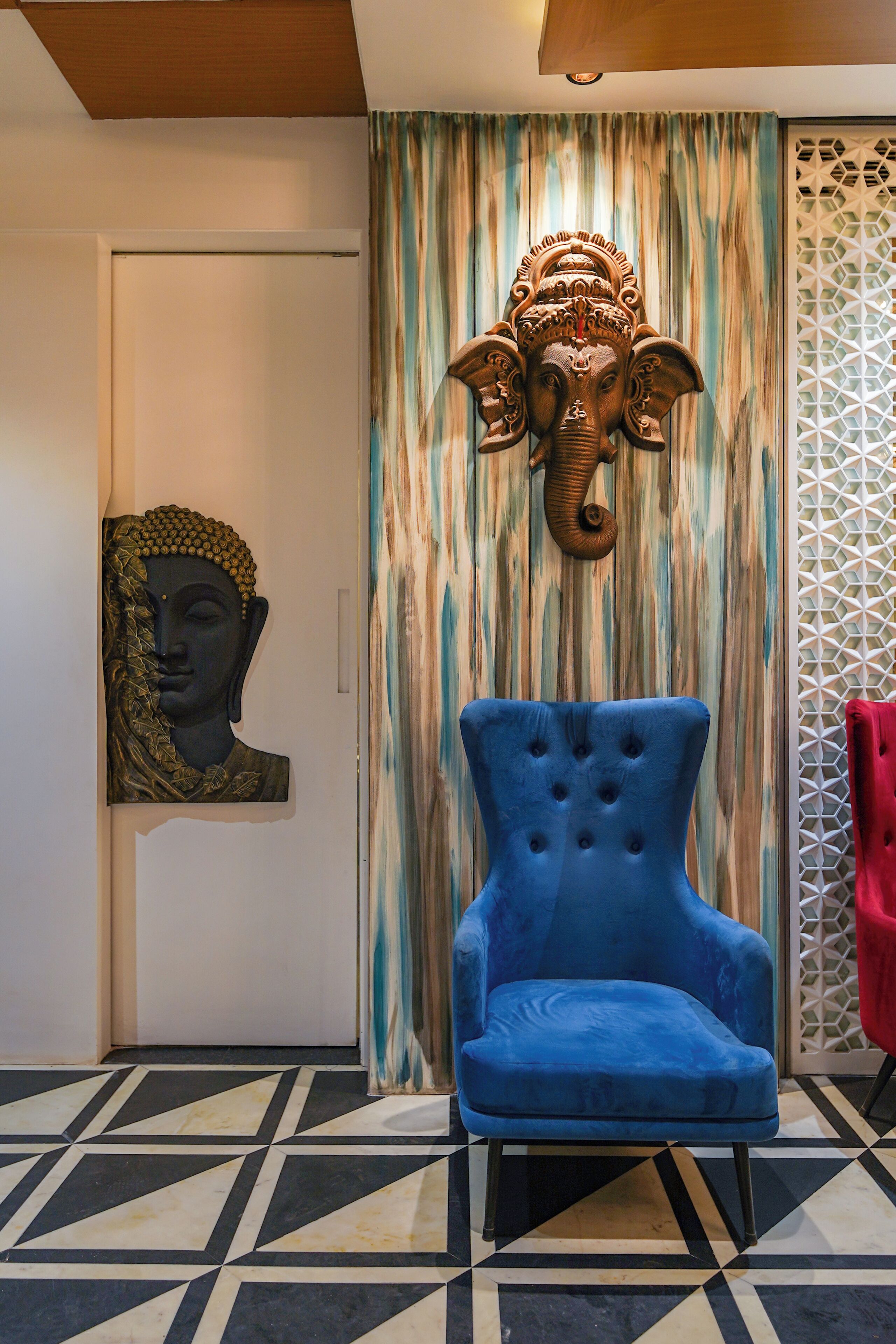 A room with a patterned floor, a blue armchair, a decorative elephant head, and a Buddha head sculpture.