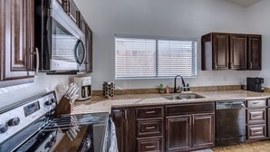 A kitchen with dark wooden cabinets, a stainless steel stove, a dishwasher, a sink, and a window with blinds.