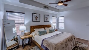 A bedroom with a bed, nightstands, a ceiling fan, and artwork on the walls.