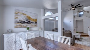 A dining area with a wooden table and white chairs, a large abstract painting on the wall, and a staircase leading to an upper level.