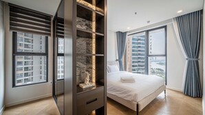 A modern bedroom with a large bed, built-in shelving, and a city view through the windows. - The LUMIERE Riverside Residence (Ho Chi Minh City)