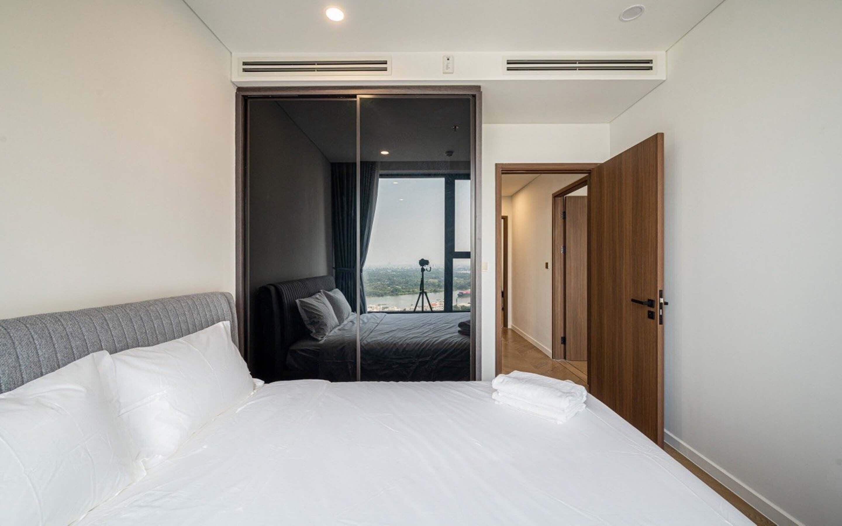 Une chambre d’hôtel avec un grand lit, une porte coulissante donnant sur un balcon équipé d’un trépied pour appareil photo, et une porte en bois.
