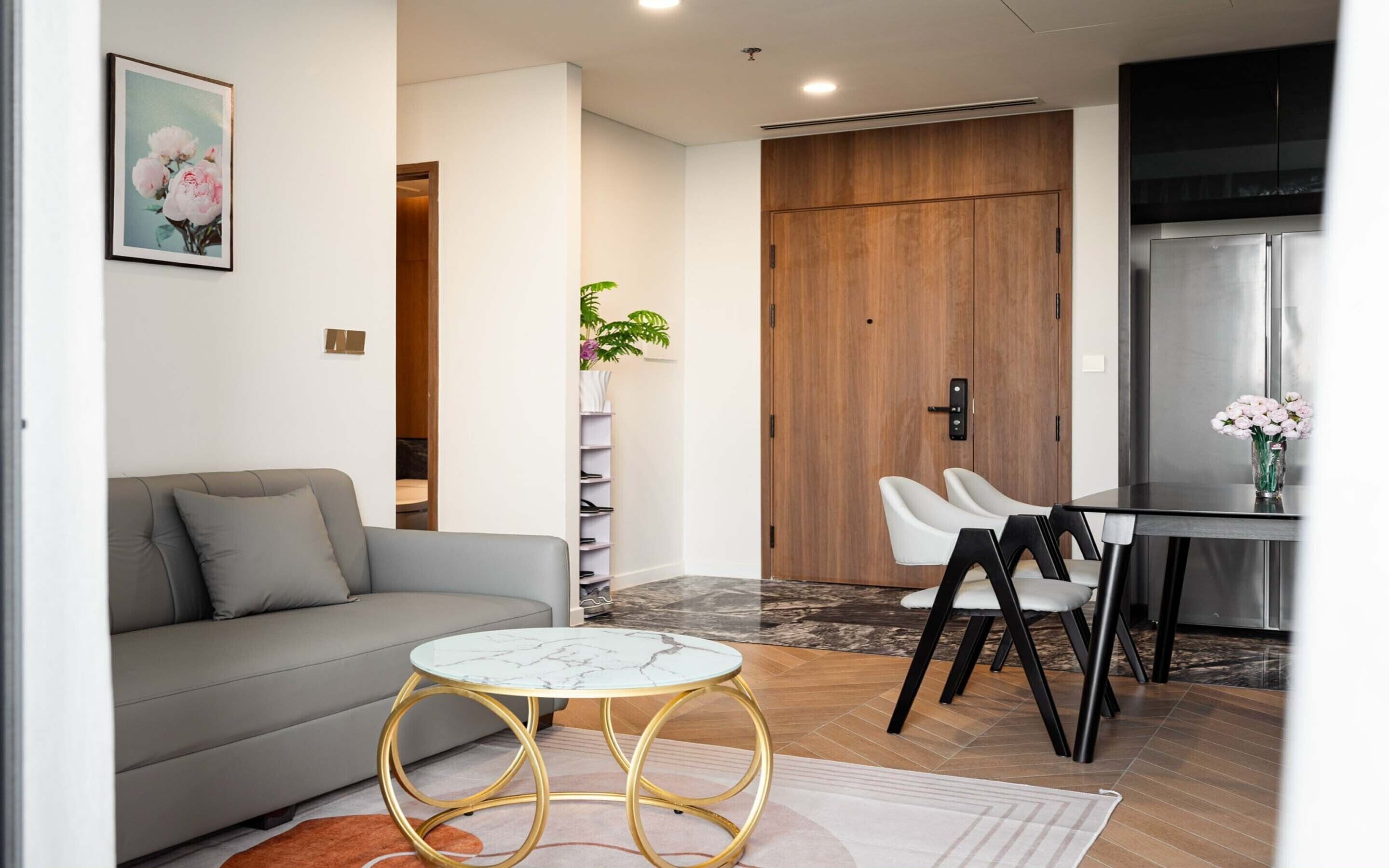 Un salon moderne avec un canapé gris, une table basse en marbre et un coin repas avec des chaises blanches.
