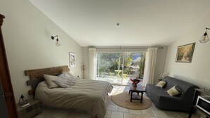 A bedroom with a bed, a sofa, a small table, and a view of the outdoors through a glass door.