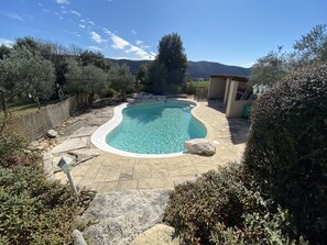 Une piscine dotée d’une plage en pierre, entourée d’arbres et offrant une vue sur les montagnes.