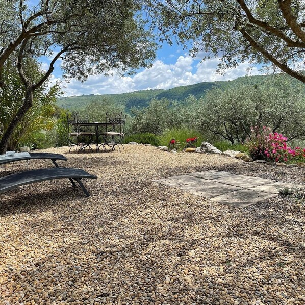 An outdoor seating area with a table and chairs, surrounded by gravel and trees.
