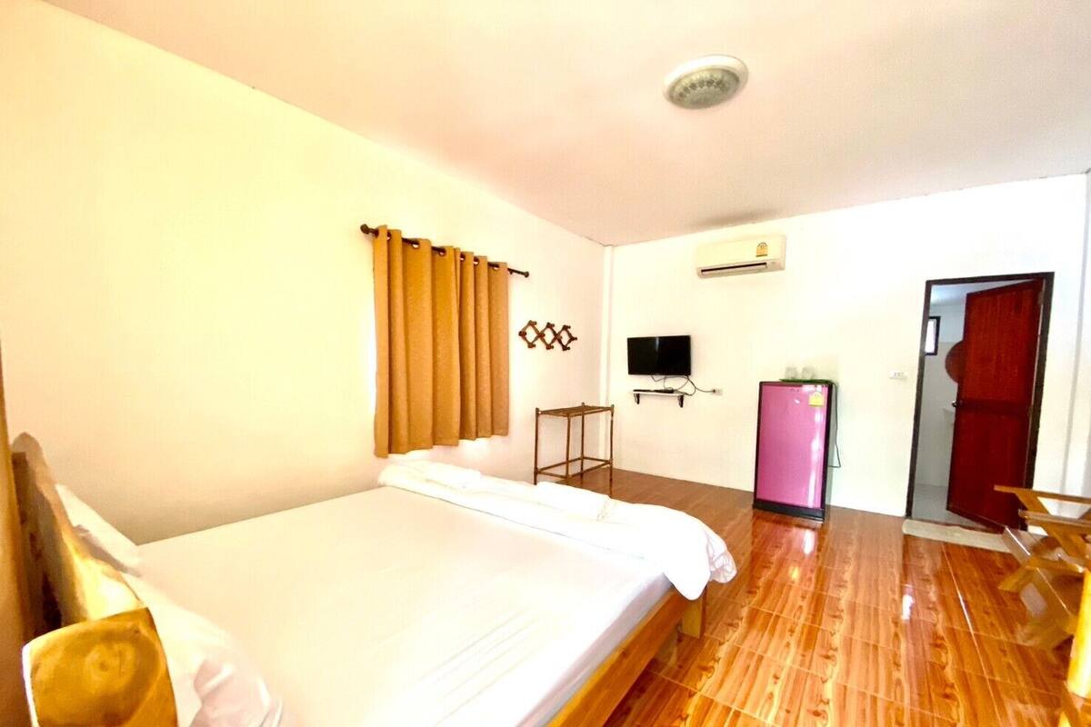 A hotel room with a bed, a TV, a refrigerator, and a door.