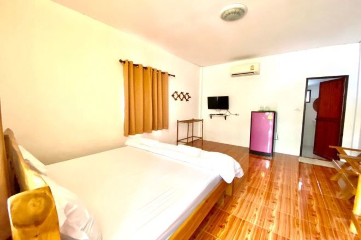 Habitación de hotel con suelo de madera, cama, televisor, refrigerador rosa y puerta al exterior.