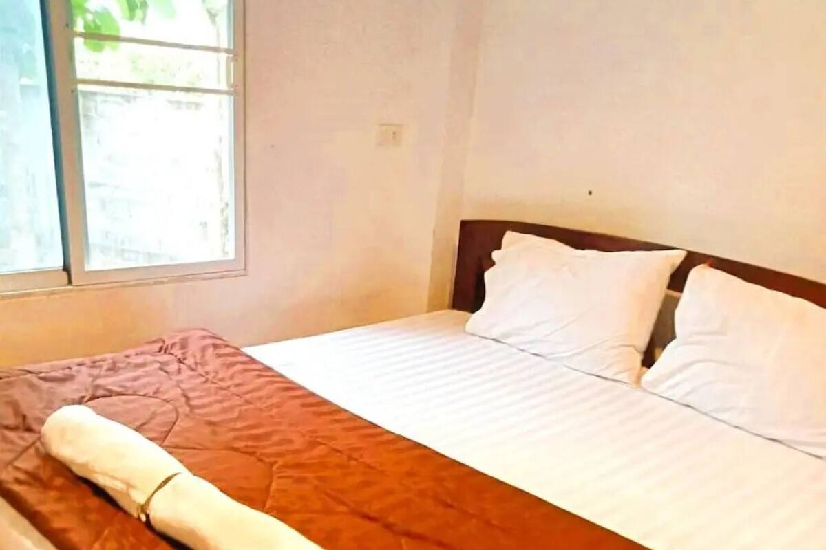 A neatly made bed with a brown bedspread and white pillows in a room with a window.