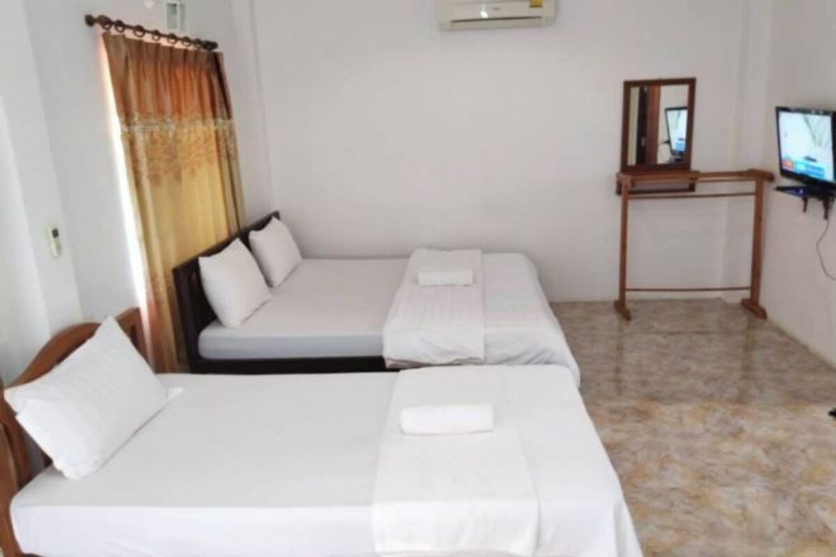 Habitación de hotel con dos camas individuales, una mesita, un televisor y un espejo.