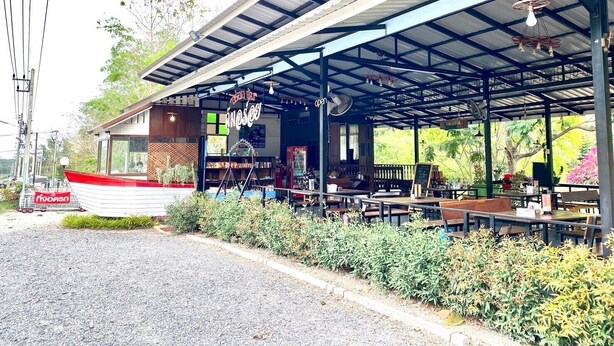 A covered outdoor seating area with tables and chairs, a small building with a sign, and a boat parked nearby.