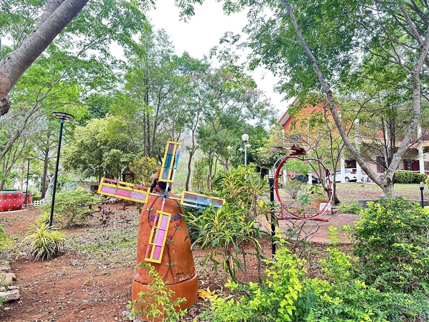 A rustic outdoor area with a wooden structure resembling a cross, surrounded by lush greenery and trees.