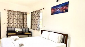 A neatly made bed with white linens, a wooden headboard, and a pillow with a unique design. There is a small table with a chair beside the bed, and a window with curtains.