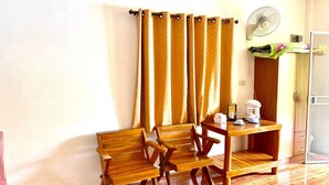 A room with a wooden floor, a wooden table with chairs, a fan, and a door.