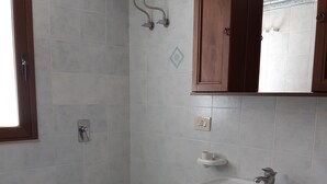 A bathroom with a toilet, bidet, sink, and a blue trash bin.