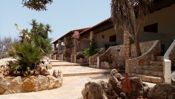 A stone building with a tiled roof, a stone staircase, and a pathway with rocks and plants.