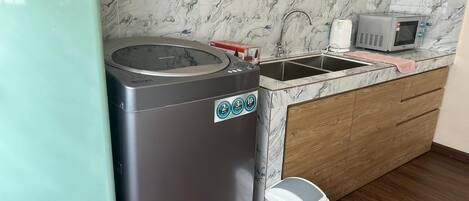 A compact kitchen with a refrigerator, a washing machine, a microwave, and a sink.