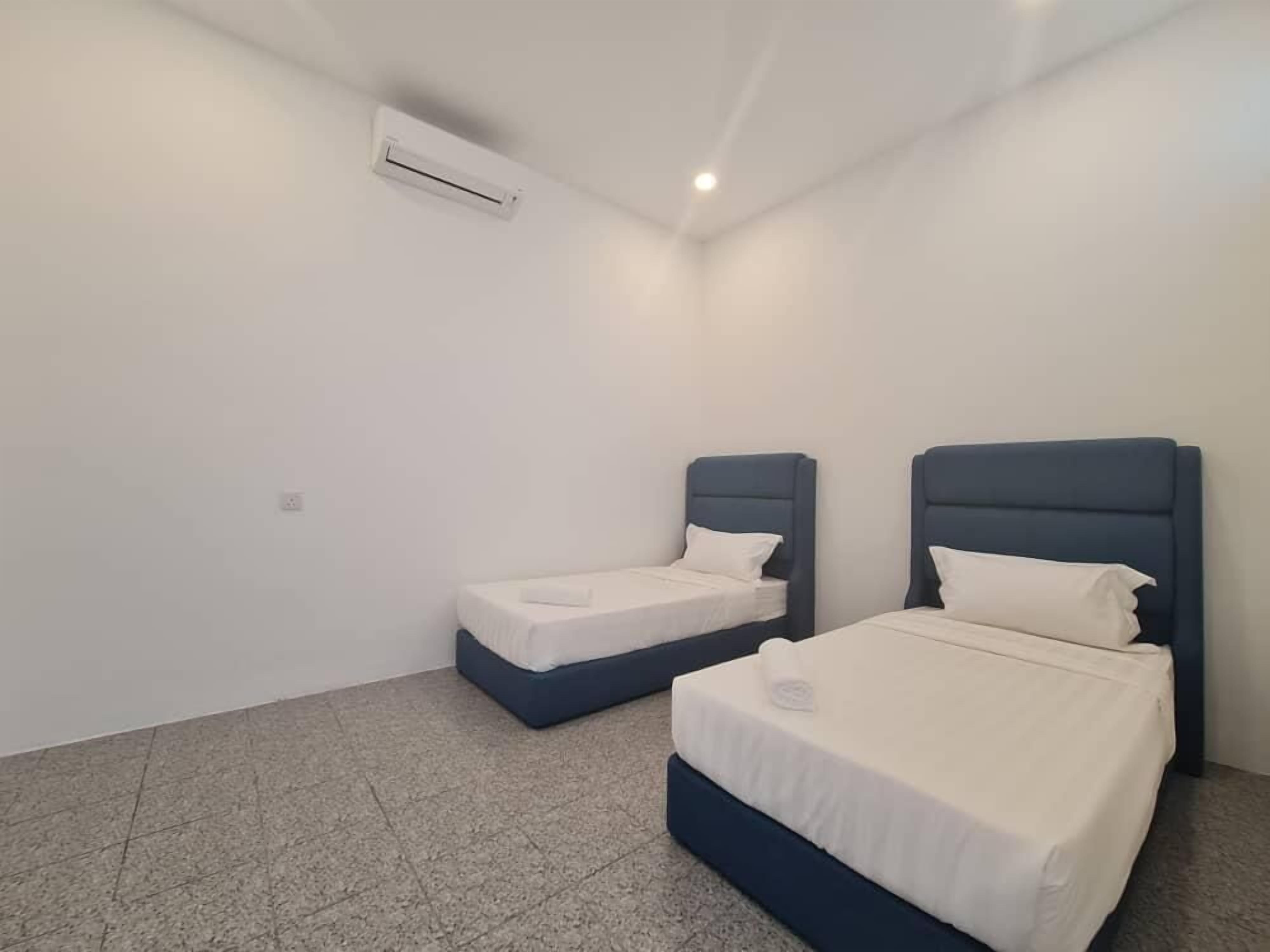 Une petite chambre propre, avec deux lits, un climatiseur blanc et un sol carrelé.