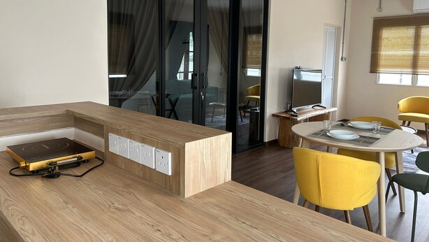 A modern kitchen with a built-in stove, a dining area with yellow chairs, and a sliding glass door leading to a living space. - Garden Home Ipoh (Ipoh)
