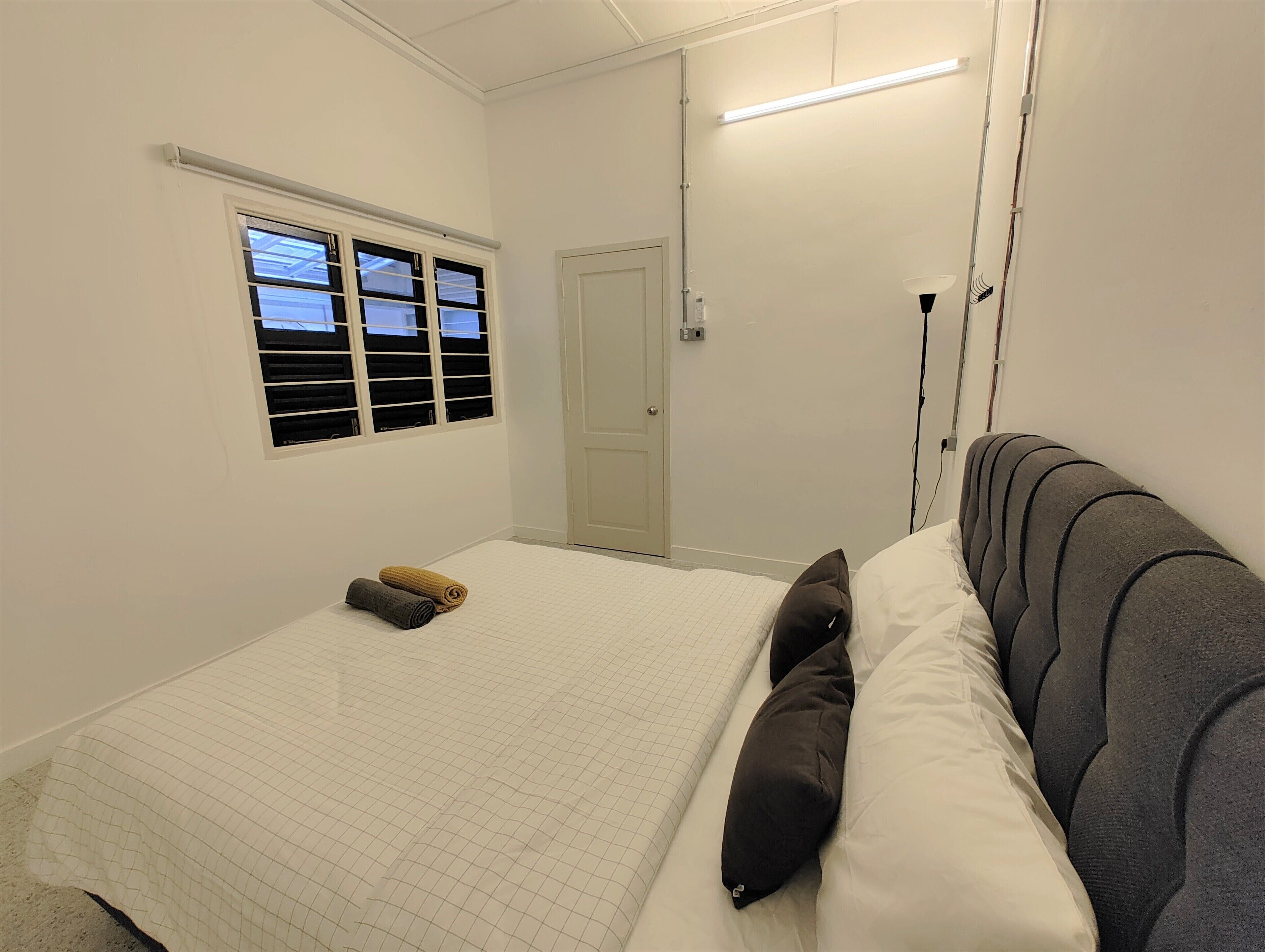 A bedroom with a bed, a window with blinds, a door, and a ceiling light.