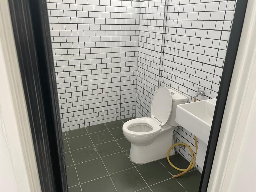 Un baño pequeño y limpio con paredes y suelo de baldosas blancas, un inodoro blanco y un lavabo blanco con manguera.