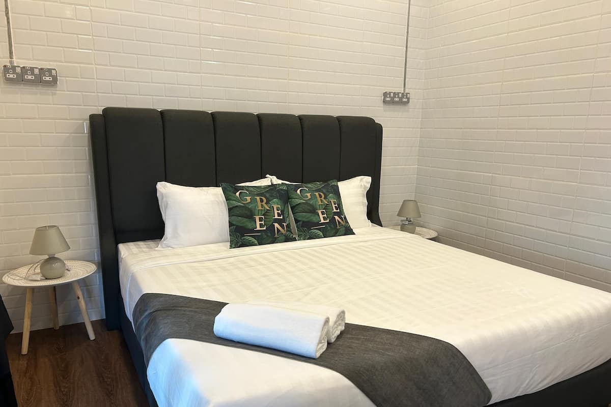 A neatly made bed with white bedding and a dark headboard, two bedside tables with lamps, and a wall with white tiles and electrical outlets.