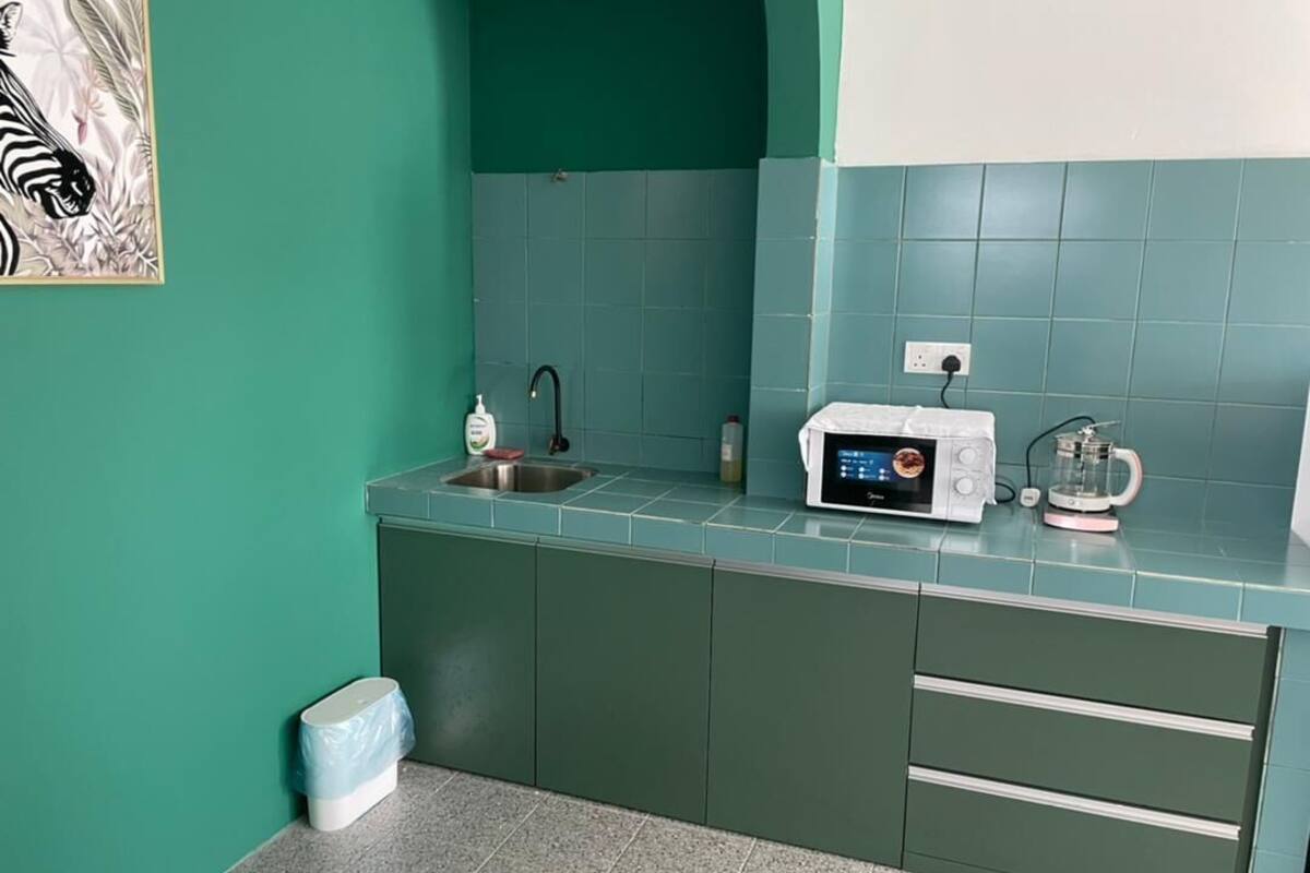 A kitchen with teal walls, a microwave, a kettle, and a sink.