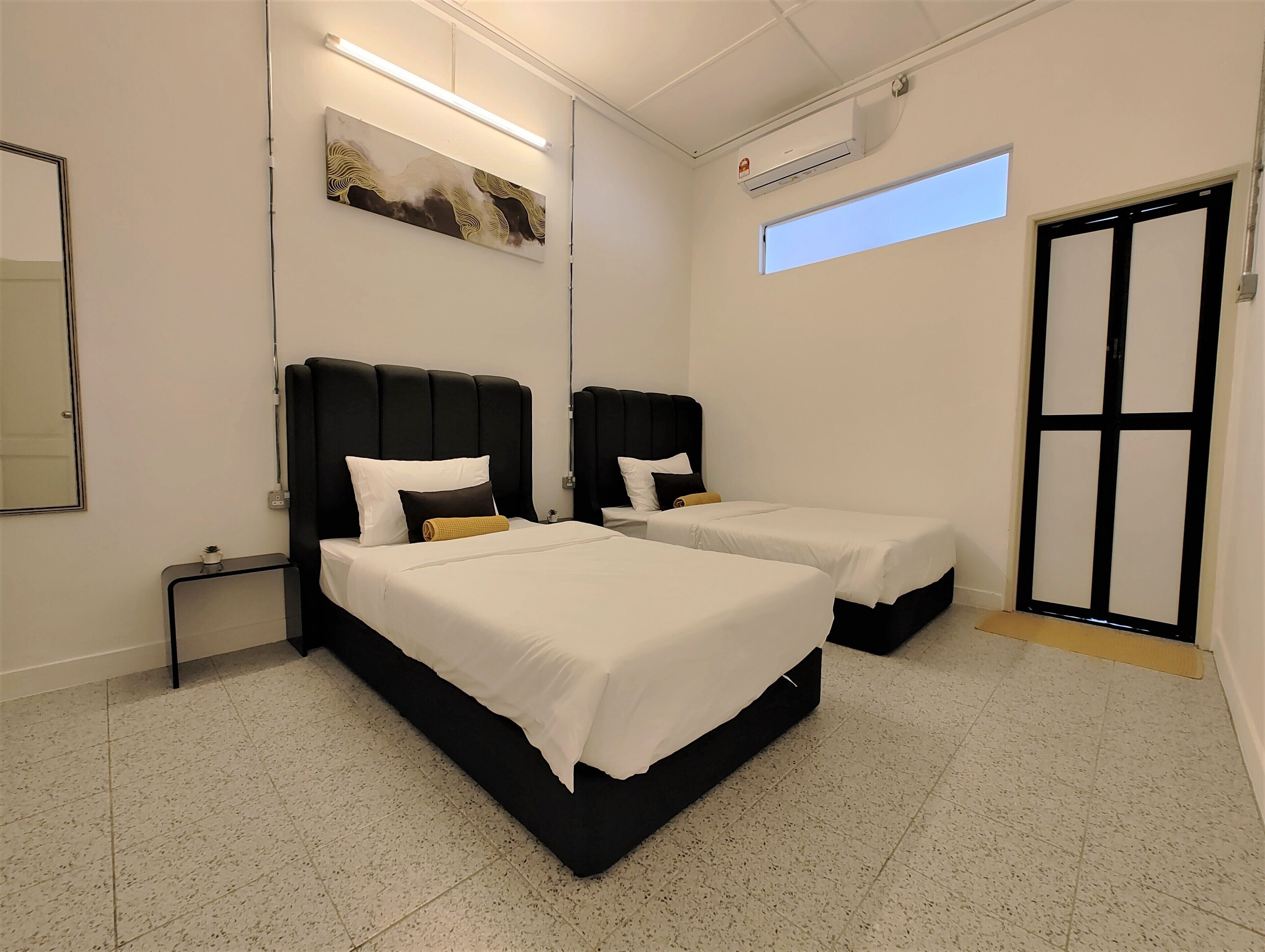 Quarto de hotel com duas camas, um espelho grande, um quadro, um aparelho de ar condicionado e uma janela.
