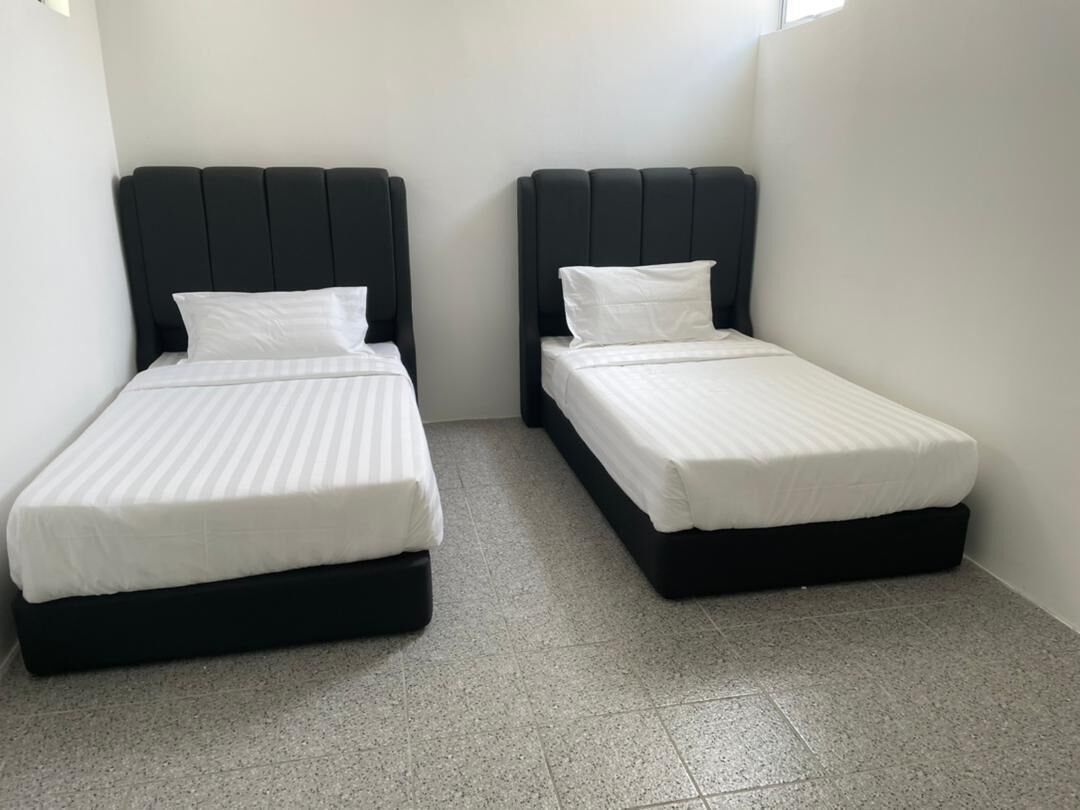 Dos camas individuales con cabeceros negros en una habitación pequeña y con suelo de baldosas.