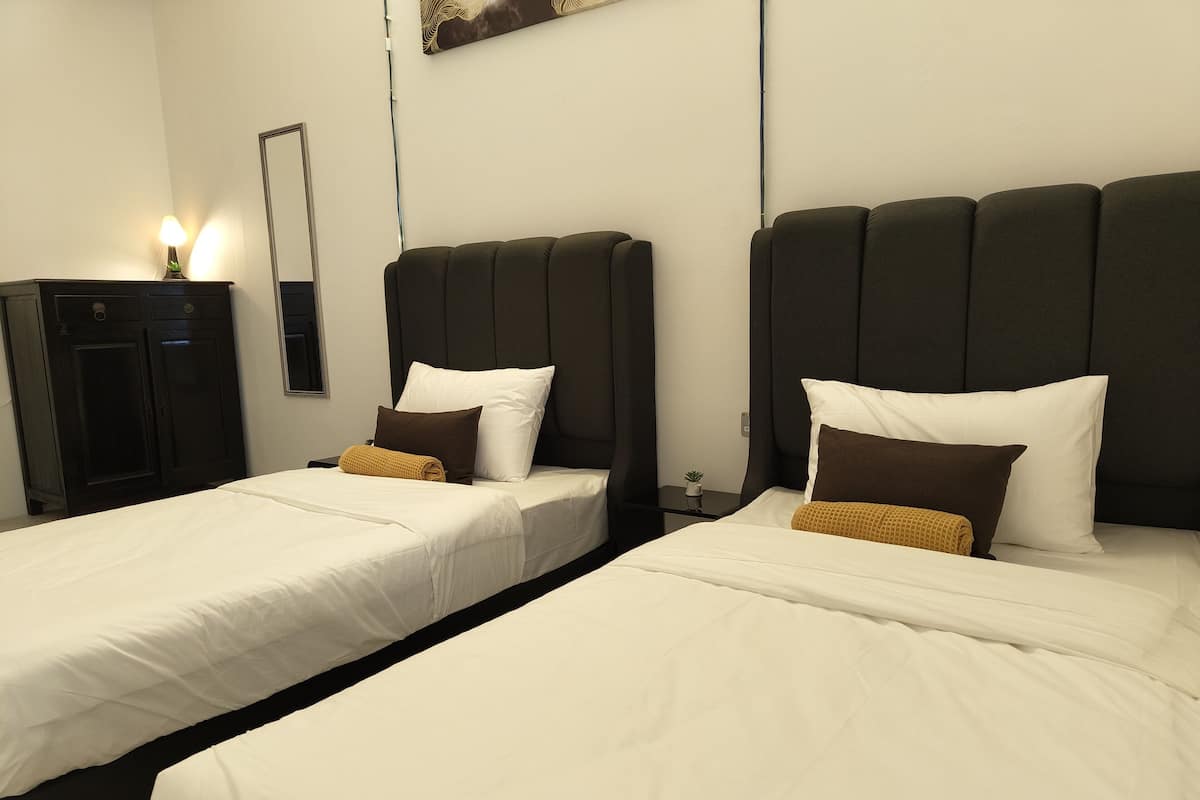 Two single beds with dark headboards, white bedding, and a small bedside table with a plant.