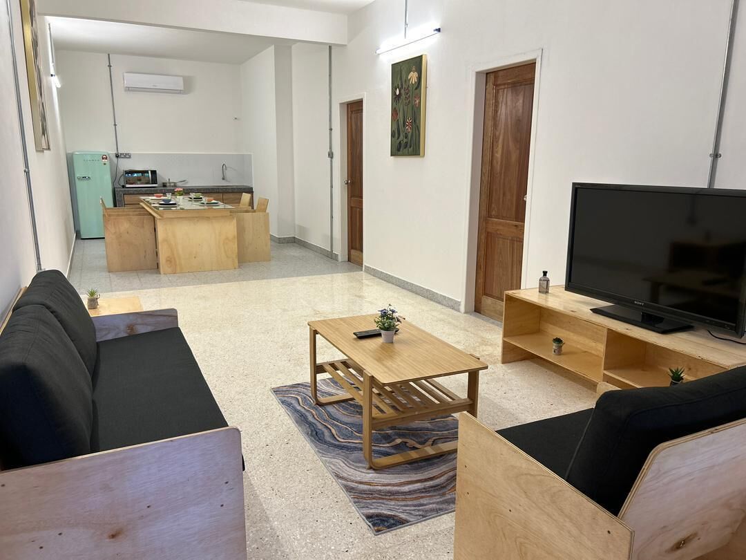 A modern living room with a sofa, a coffee table, a TV, and a kitchen area in the background.