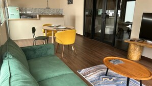 A modern living room with a green sofa, yellow chairs, a wooden coffee table, and a kitchen area with a refrigerator and stove. - Garden Home Ipoh (Ipoh)