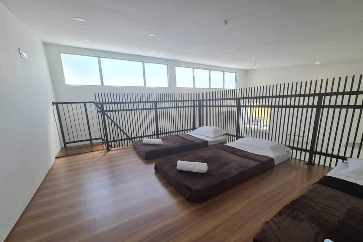 A modern room with two beds, a wooden floor, a black metal railing, and large windows.