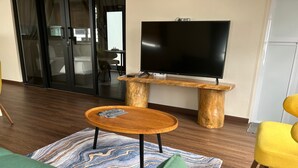 A modern living room with a flat-screen TV on a wooden stand, a round wooden coffee table, and a green sofa. - Garden Home Ipoh (Ipoh)