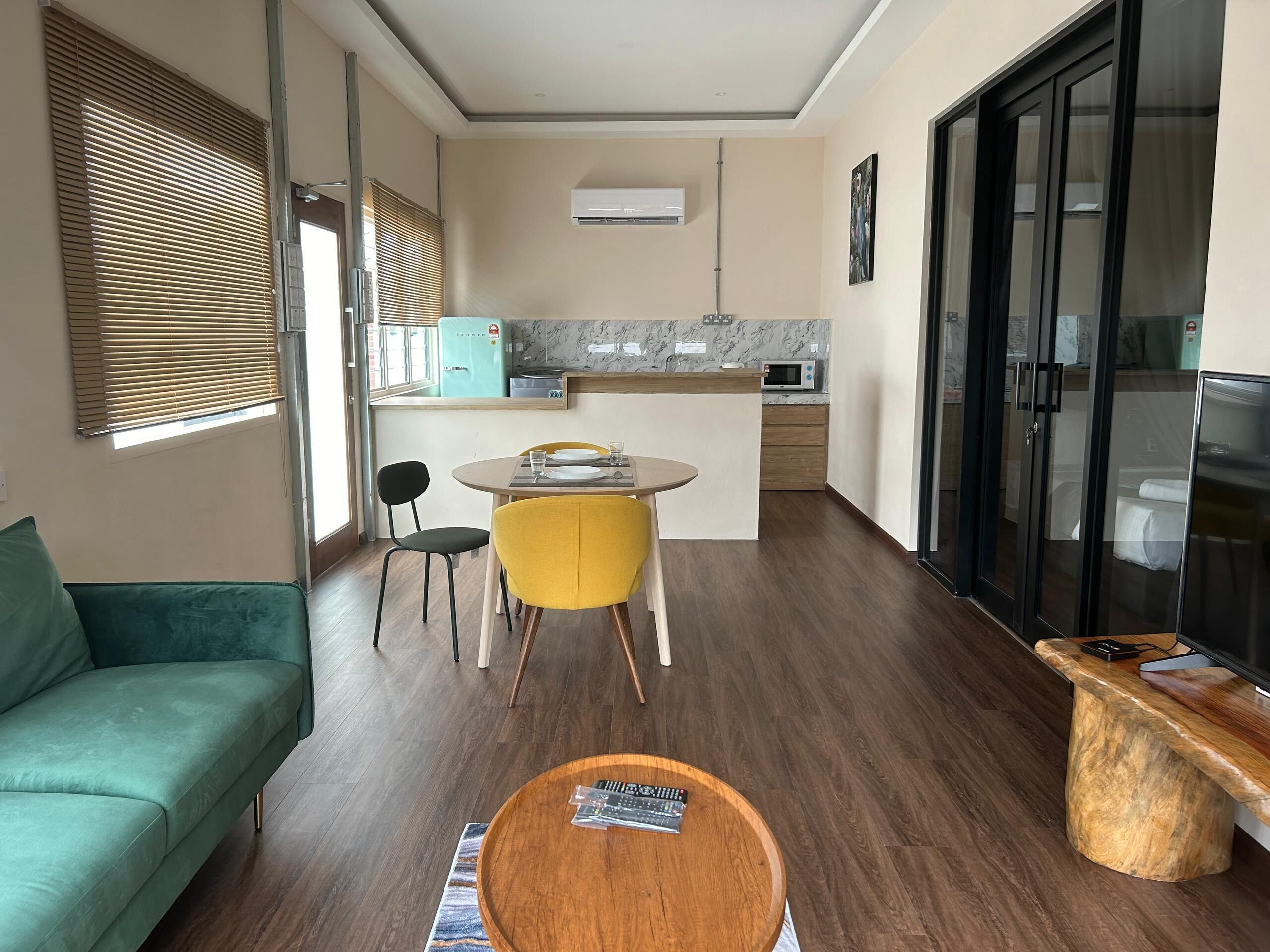 Un espacio habitable compacto con sofá, una mesa de comedor con sillas, una zona de cocina con microondas y un televisor.