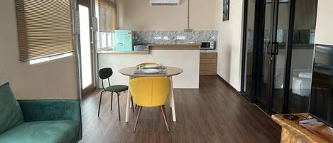 Un espacio habitable compacto con sofá, una mesa de comedor con sillas, una zona de cocina con microondas y un televisor.