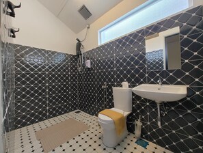 Une salle de bain avec des carreaux hexagonaux noirs et blancs, des toilettes blanches, un lavabo et un espace douche.
