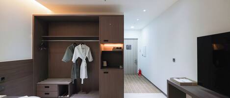 A modern hotel room with a bed, a walk-in closet, a TV, and a small kitchenette.