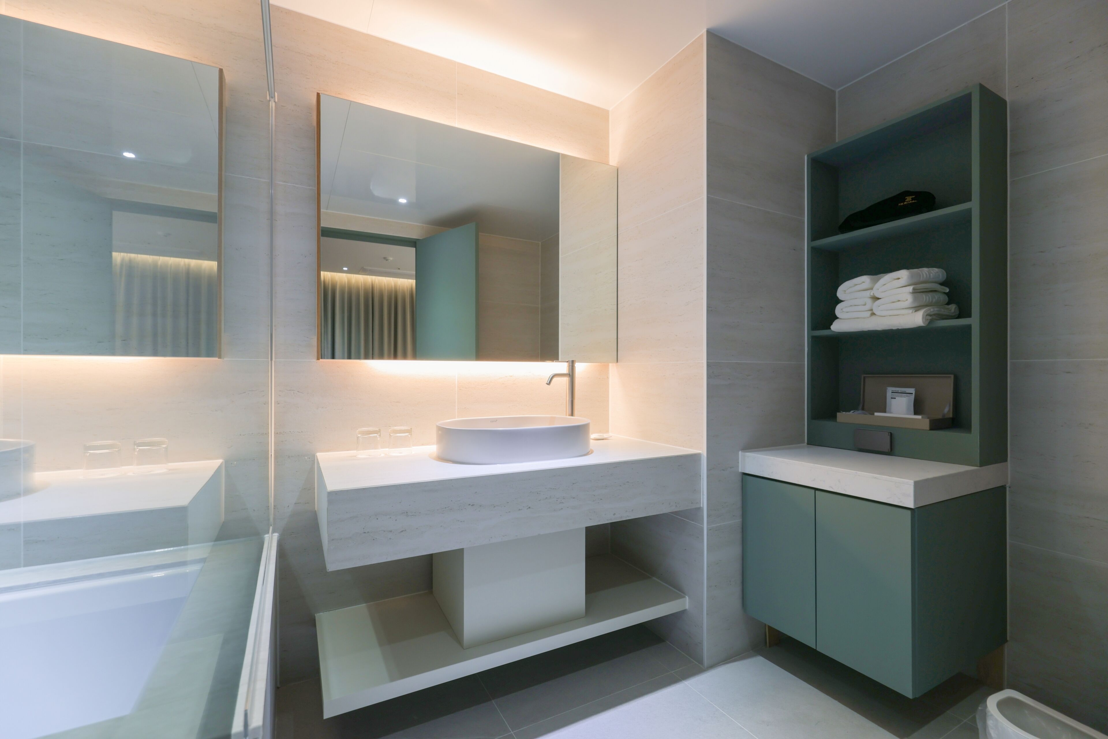 A modern bathroom with a glass-enclosed shower, a white sink with a large mirror, and a green vanity with shelves.